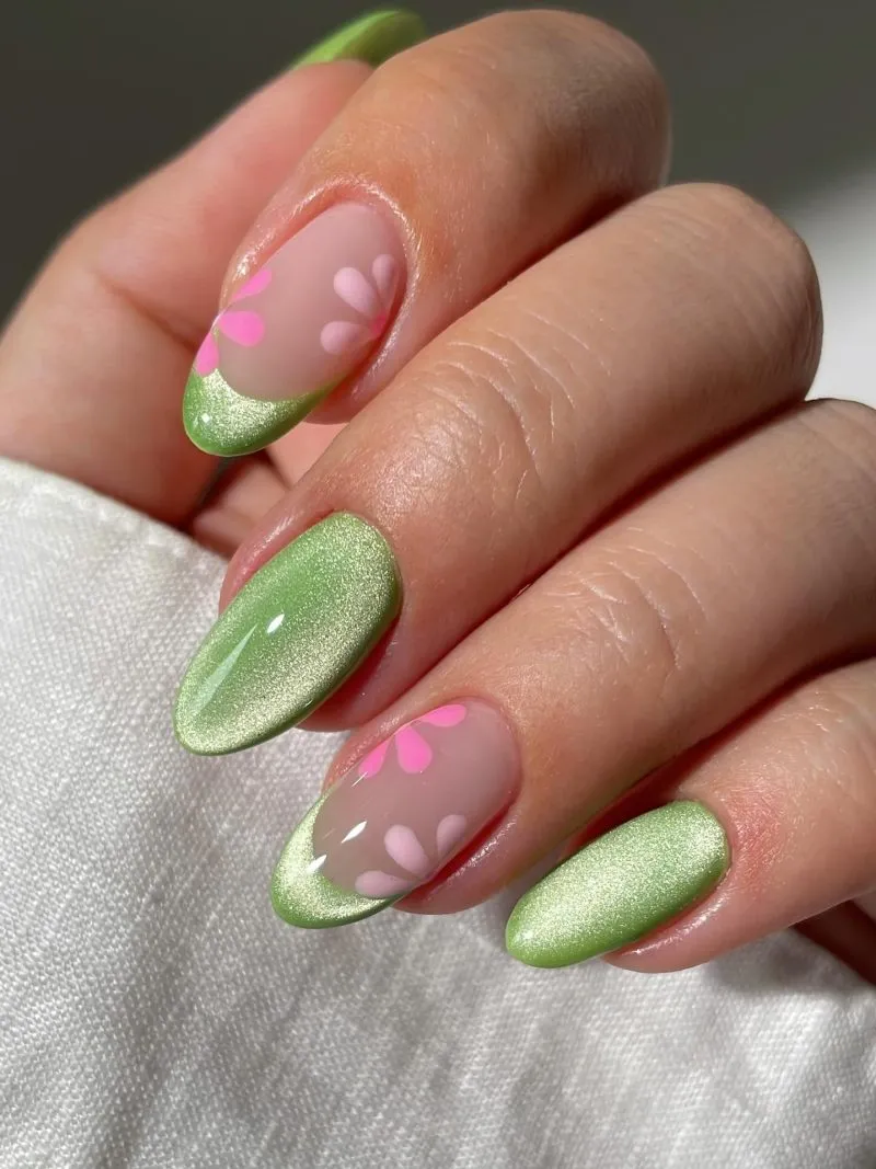 Green floral nails with cat eye effect and pink flowers - fresh hand showcasing green cat eye base with pink flower petals, featuring green leaves and stems on almond-shaped nails